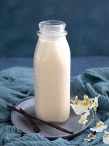 A glass bottle filled with homemade low carb coffee creamer with a vanilla pod and white orchid next to it
