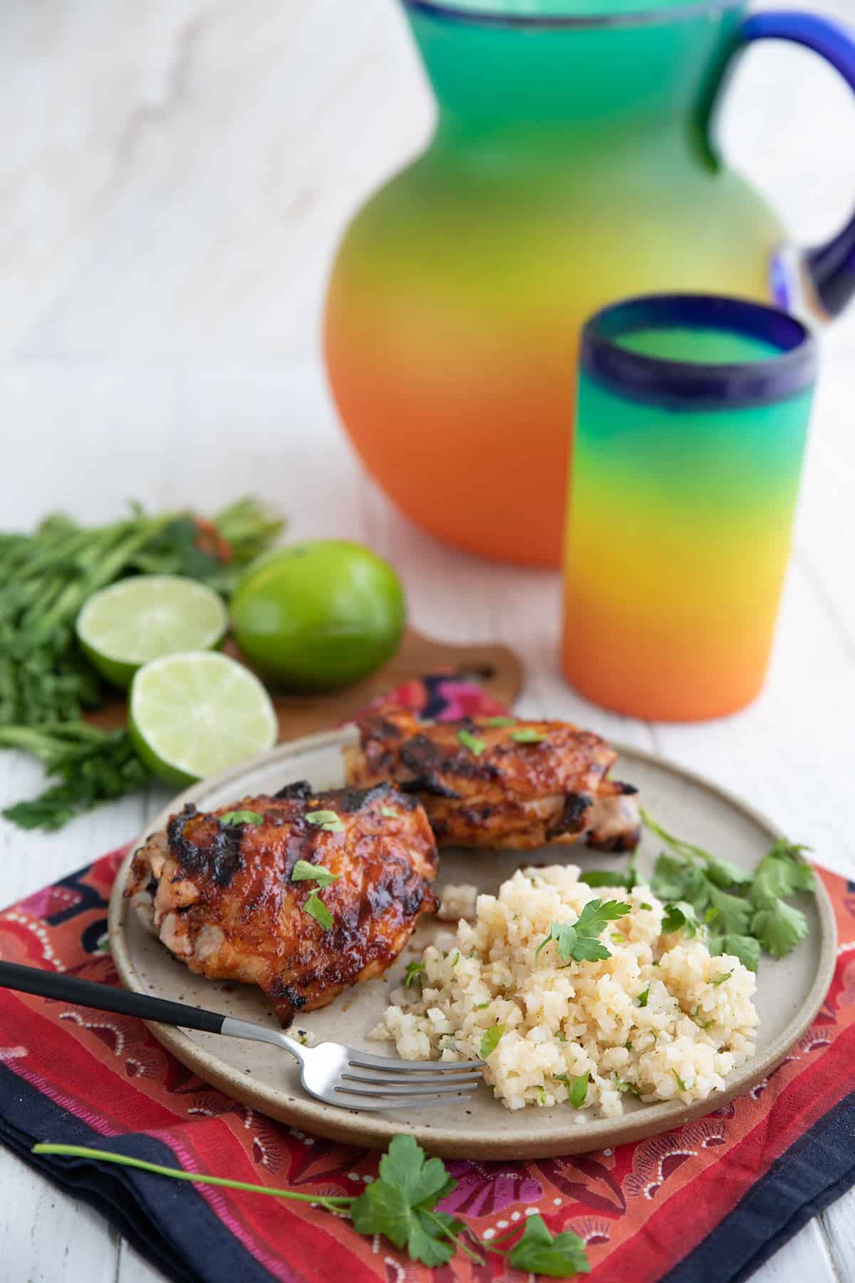 A plate with chicken and Cilantro Lime Cauliflower Rice in front of a Mexican glass jug.