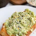 Titled image of a slice of keto avocado toast on a white plate with everything bagel seasoning on top.