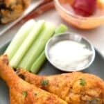 Titled image of two pieces of crispy baked buffalo chicken on a black plate with celery sticks.