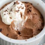 Close up shot of a white ramekin filled with keto chocolate mousse, with a dollop of whipped cream on top.