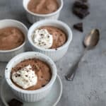 4 white dessert cups filled with sugar-free keto chocolate mousse and topped with whipped cream and chocolate shavings.