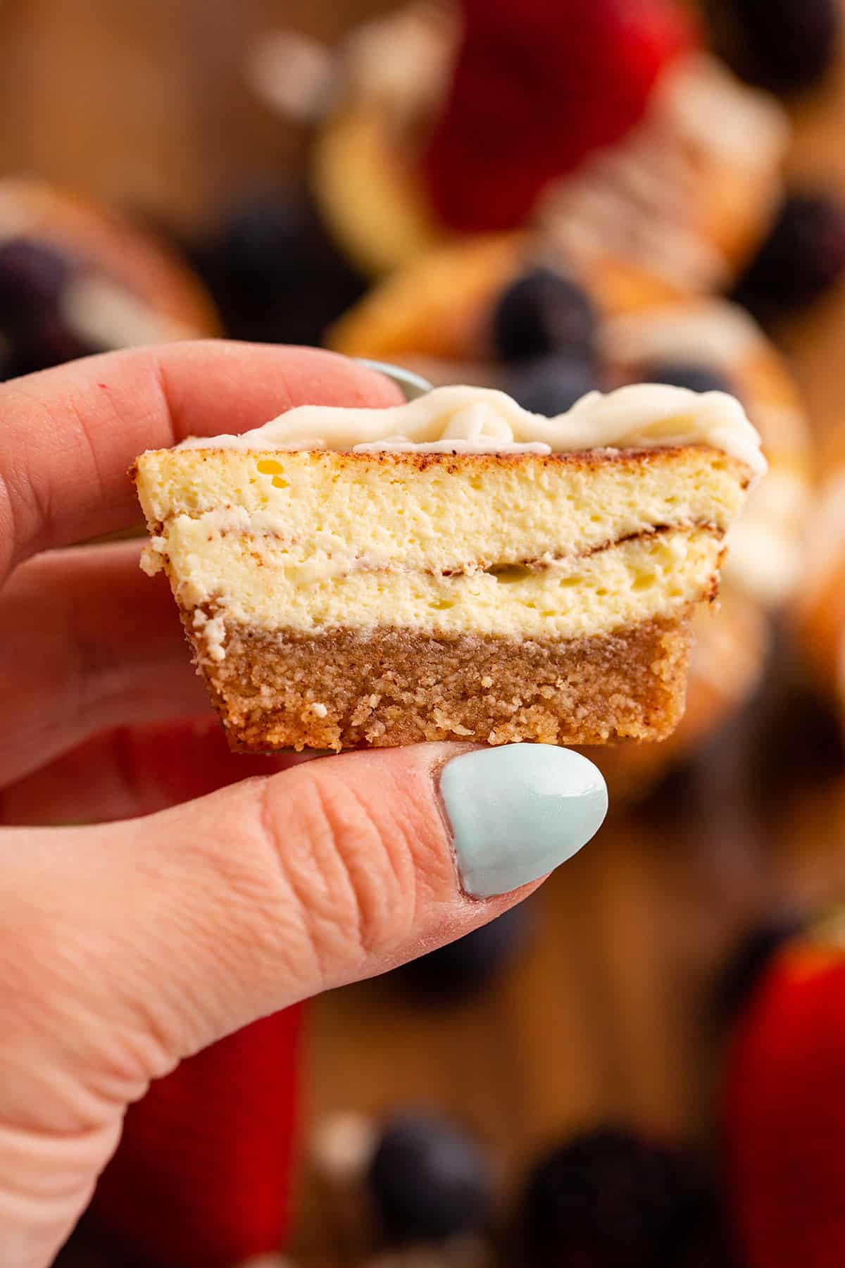 A hand holding up a cinnamon roll cheesecake, cut open to show the inside.