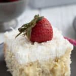 A slice of Keto Coconut Cream Poke Cake on a dark gray plate over a pink patterned napkin.