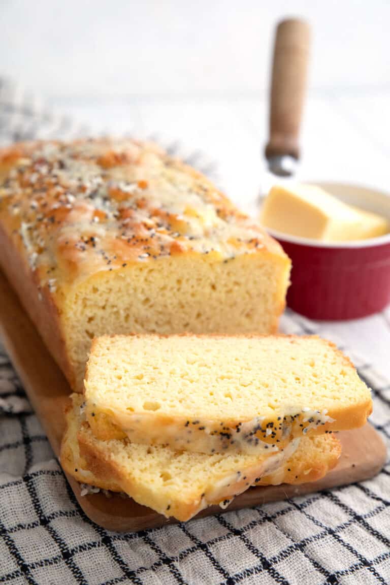 A loaf of coconut flour bread on a plaid cloth with several slices cut and laid in front.