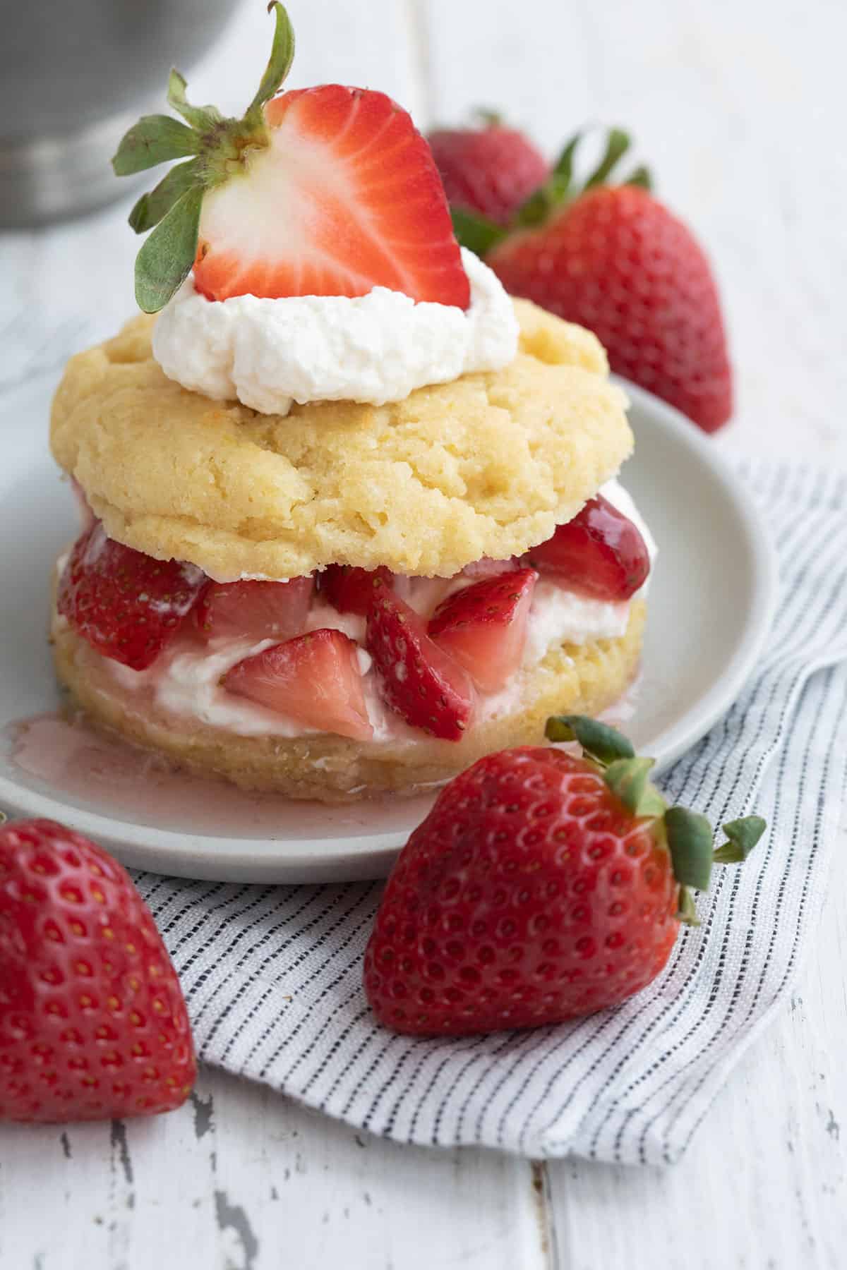 Keto Strawberry Shortcake on a gray plate over a striped napkin, with fresh strawberries strewn around.
