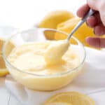 A hand spooning keto lemon curd out of a glass bowl.