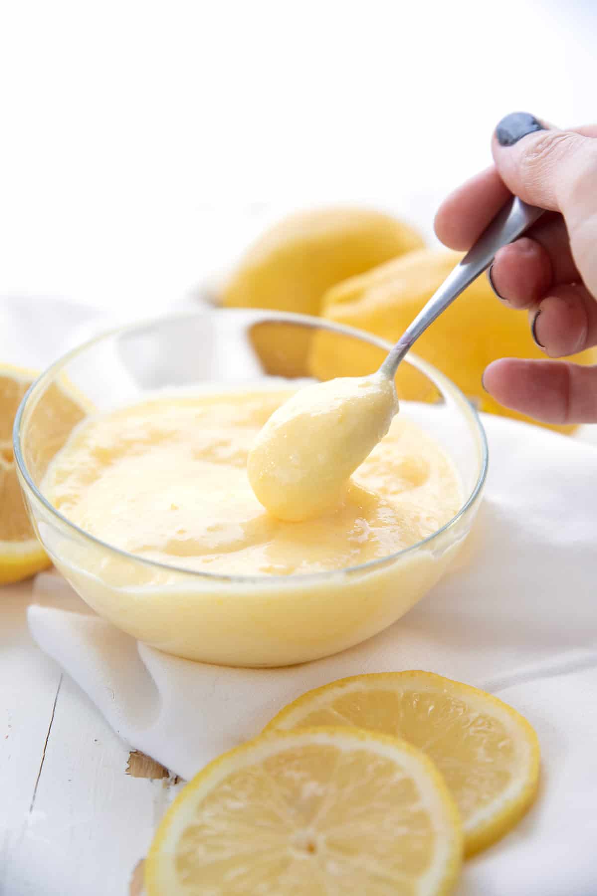 A hand spooning keto lemon curd out of a glass bowl.