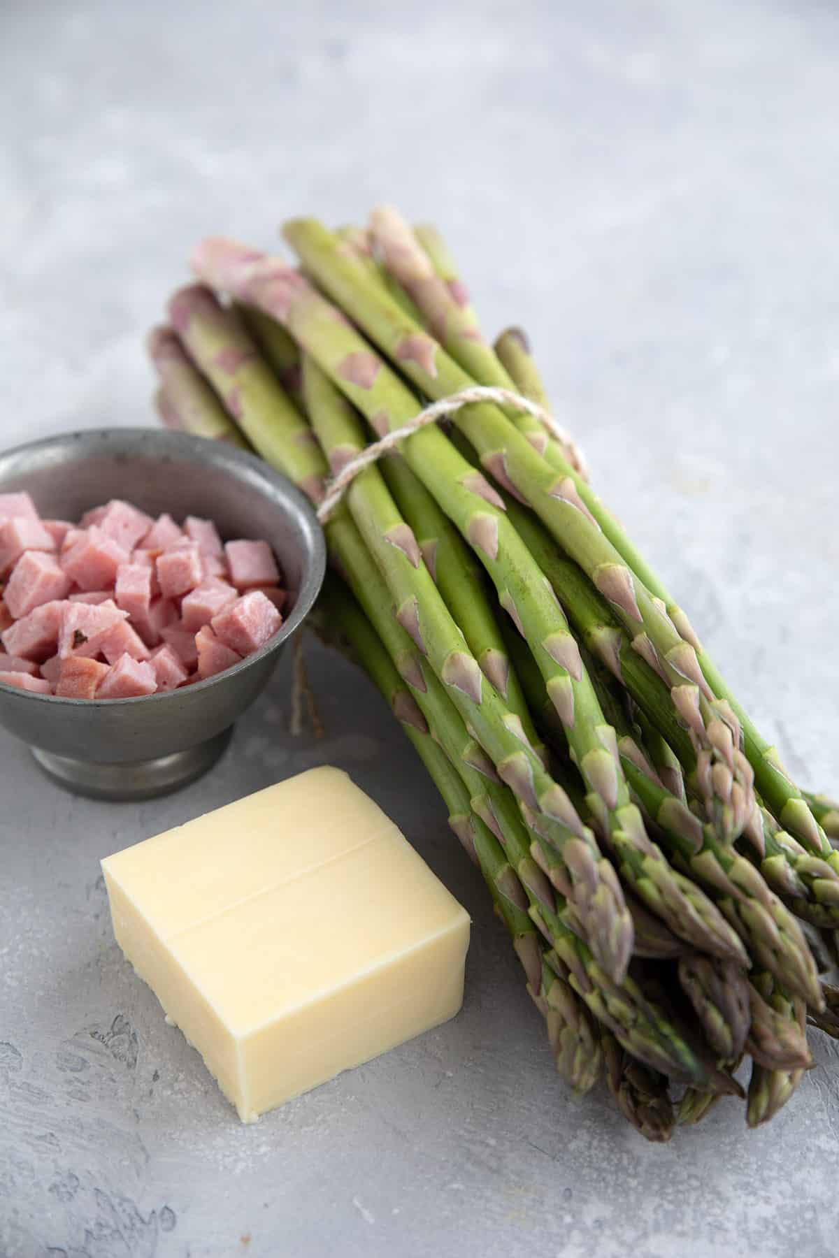 Asparagus, ham, and cheese on a gray table.