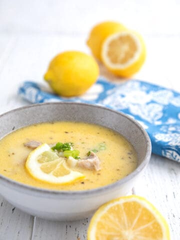 A bowl of Lemon Chicken Soup (Avgolemono) with lemons and a blue napkin.