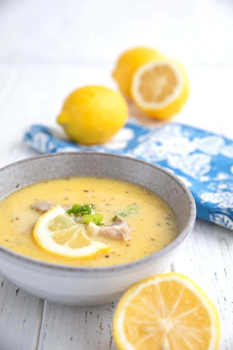 A bowl of Lemon Chicken Soup (Avgolemono) with lemons and a blue napkin.