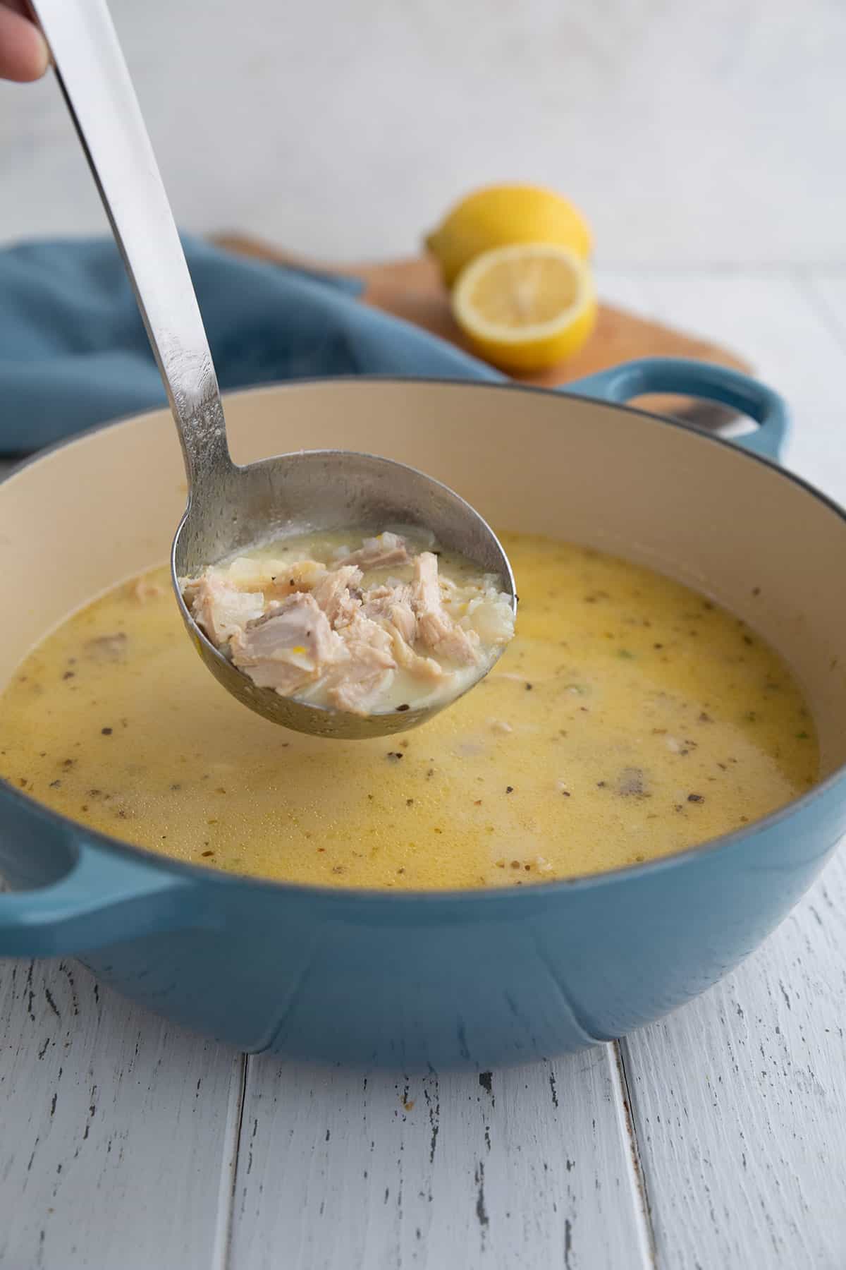 A ladle full of lemon chicken soup lifted above a blue pot.