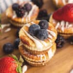 Mini Cinnamon Roll Cheesecakes with berries on top on a wooden cutting board.