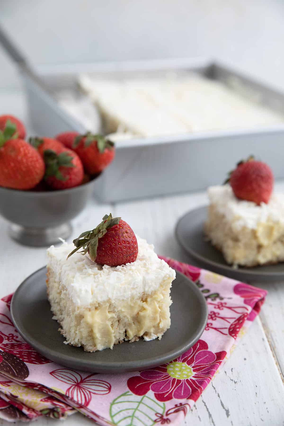 Two slices of Keto Coconut Cream Poke Cake with strawberries on top.
