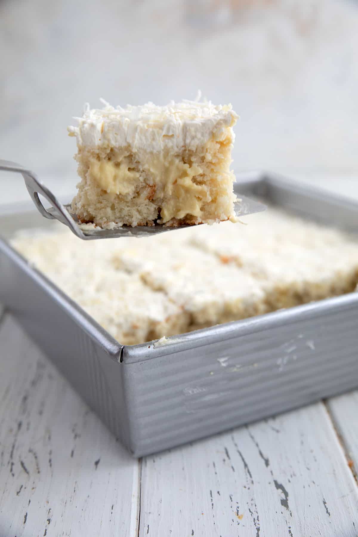 A spatula lifting a slice of Coconut Cream Poke Cake out of the pan.