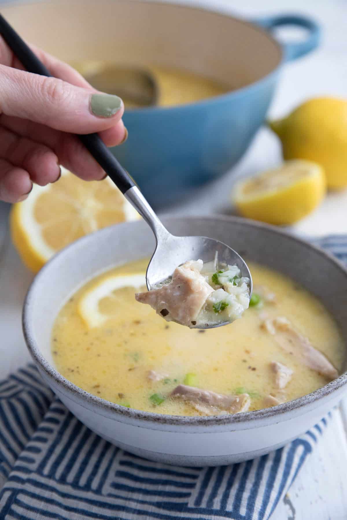 A soup spoon lifting some Keto Lemon Chicken Soup out of a bowl.