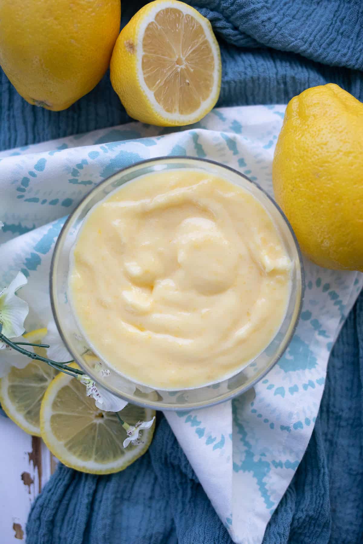 Top down image of a glass bowl filled with keto lemon curd, surrounded by lemons.