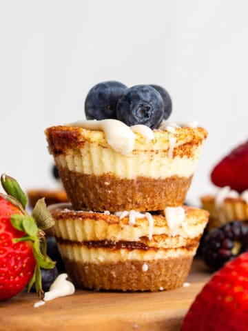 Two Mini Keto Cheesecakes piled up on a wooden cutting board with berries on top.