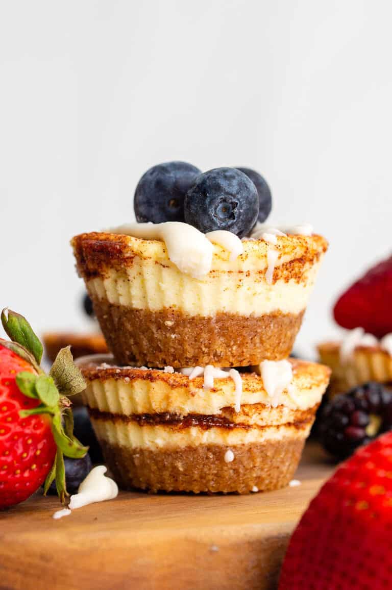 Two Mini Keto Cheesecakes piled up on a wooden cutting board with berries on top.