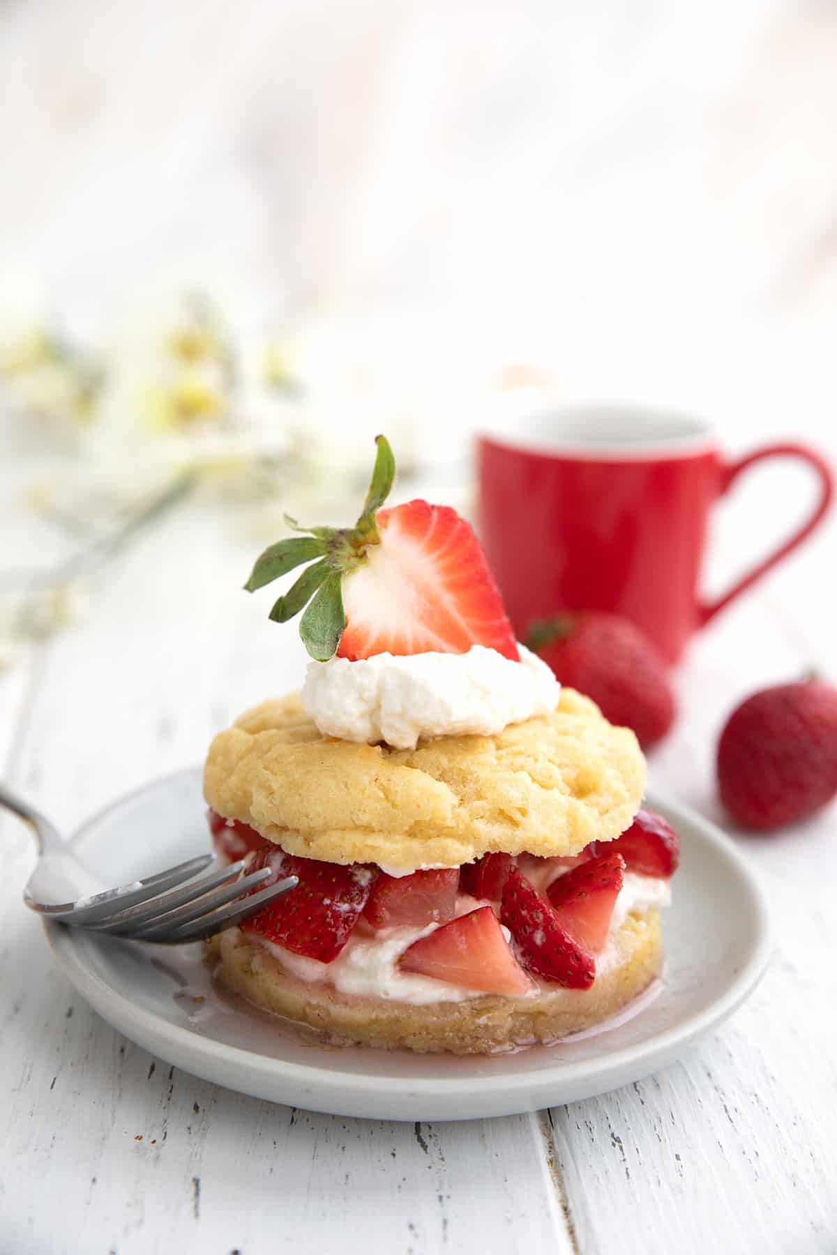 Keto Strawberry Shortcake on a white wooden table with a red cup of coffee in the background.