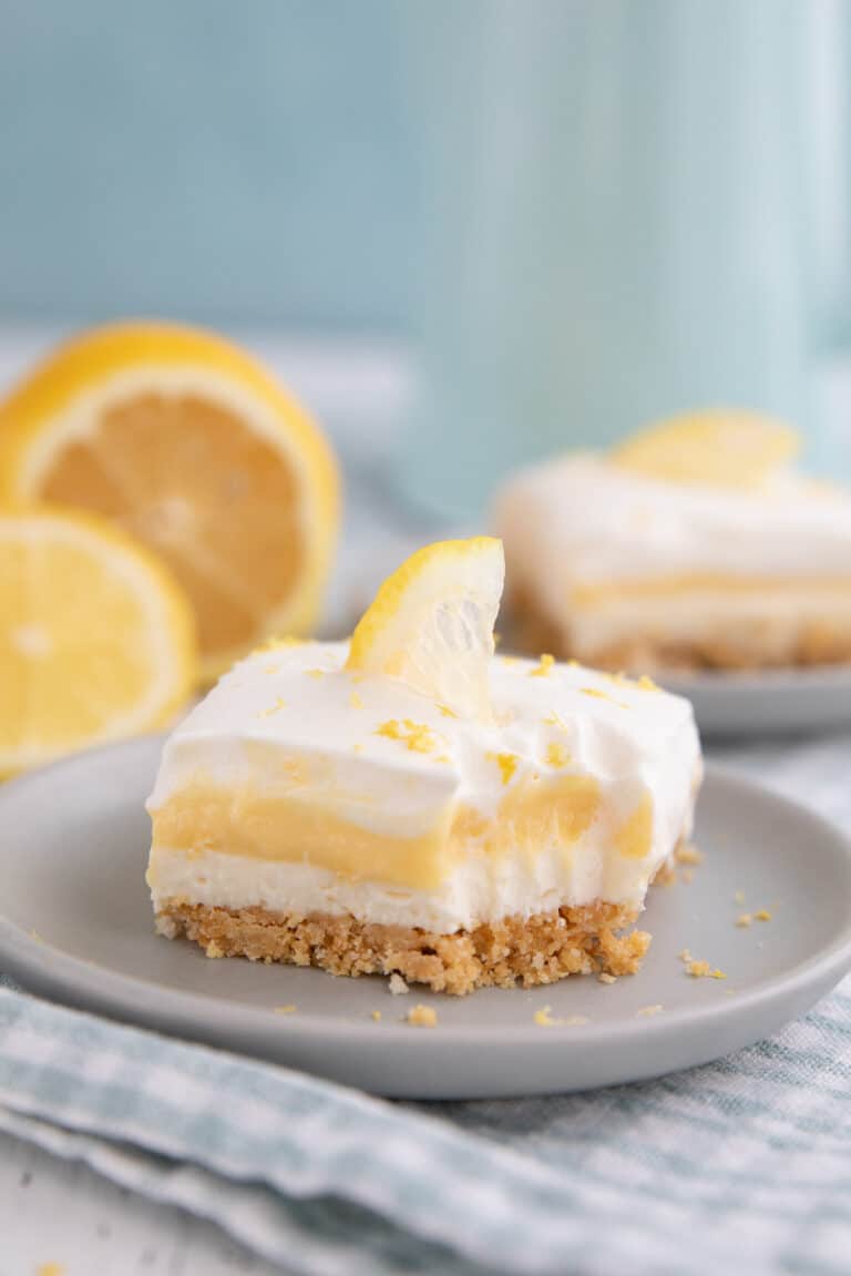 A slice of keto lemon lush on a gray plate with a forkful taken out of it.