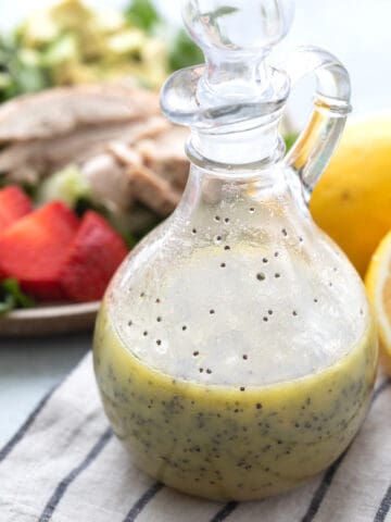 Keto Lemon Poppy Seed Dressing in a glass dressing container on a striped napkin.