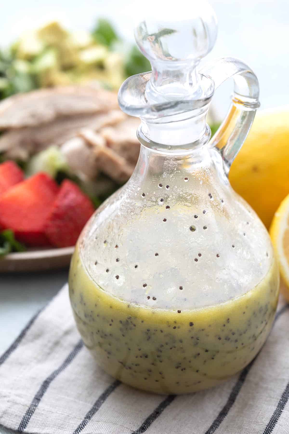 Keto Lemon Poppy Seed Dressing in a glass dressing container on a striped napkin.