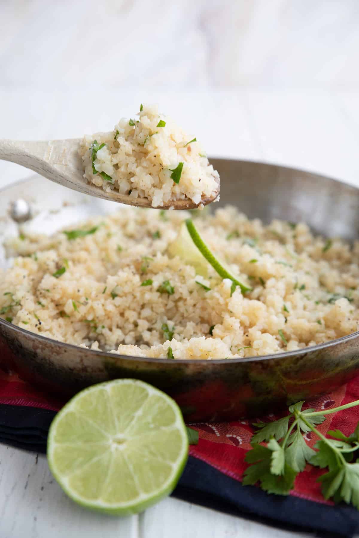 A wooden spoon lifting Keto Cilantro Lime Cauliflower Rice out of the skillet.