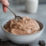 A bowl full of sugar free keto chocolate mousse with a spoon reaching into it.