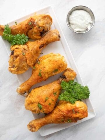 Top down image of pieces of baked Buffalo chicken on a white platter with a small bowl of ranch dressing.