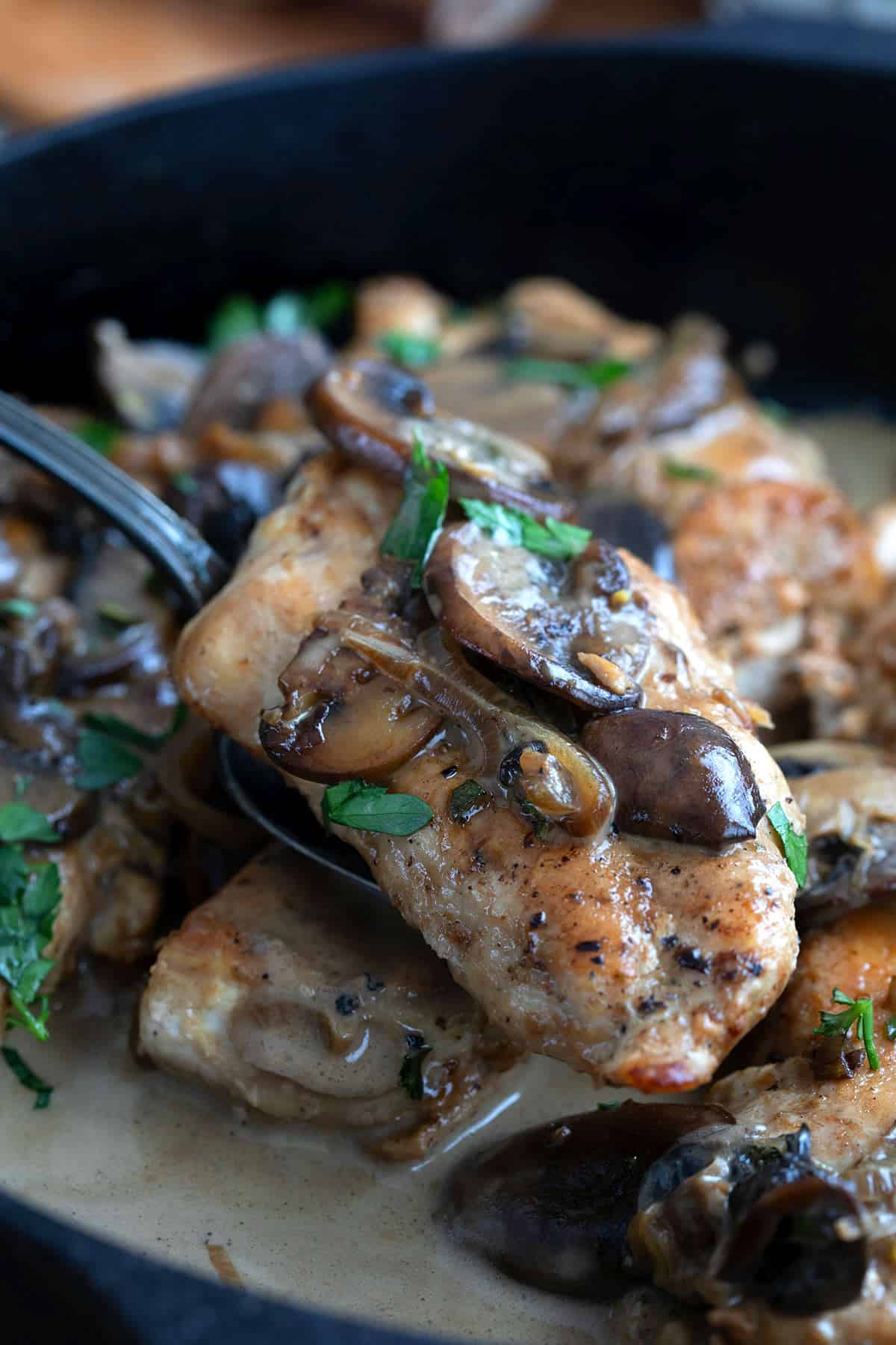 A serving spoon lifting a piece of Keto Chicken Marsala out of the pan.