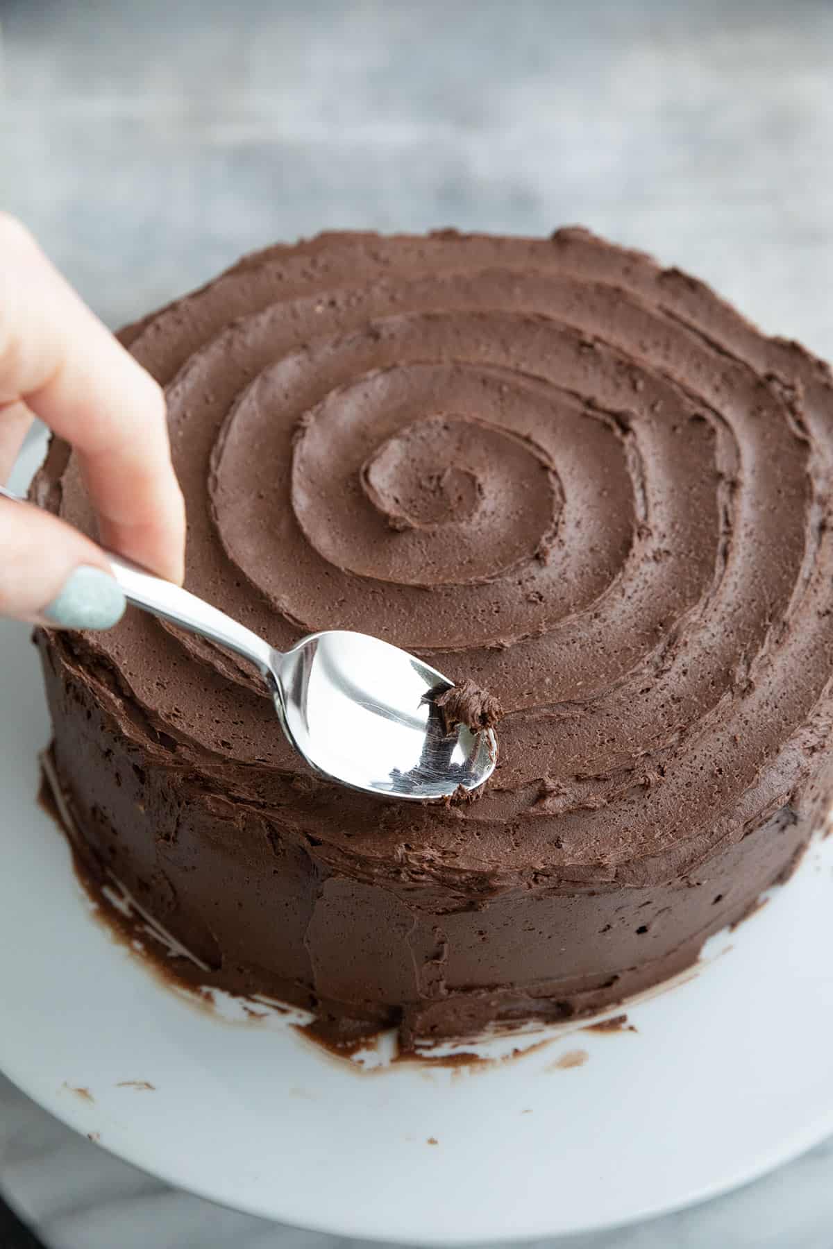 A spoon creating a swirl design on a keto chocolate cake.