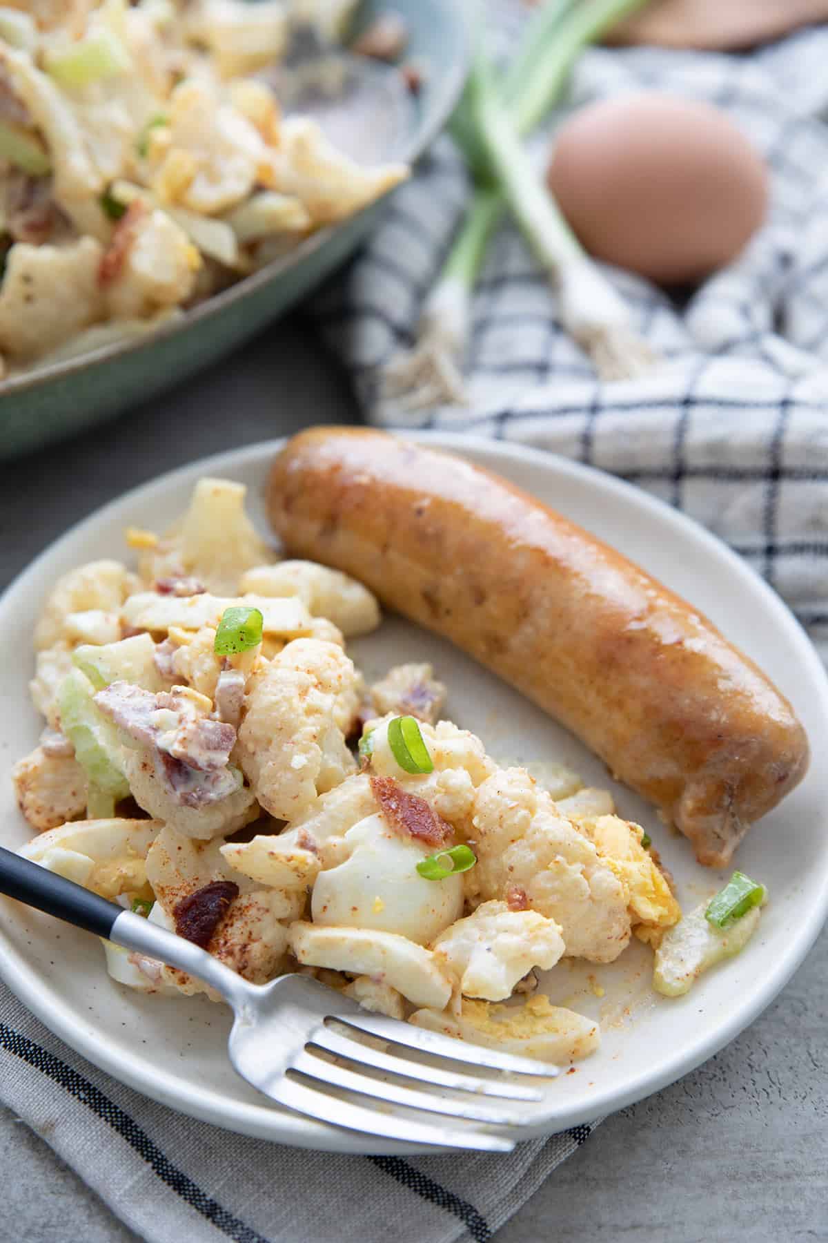 Cauliflower salad on a plate with a grilled sausage and a fork.