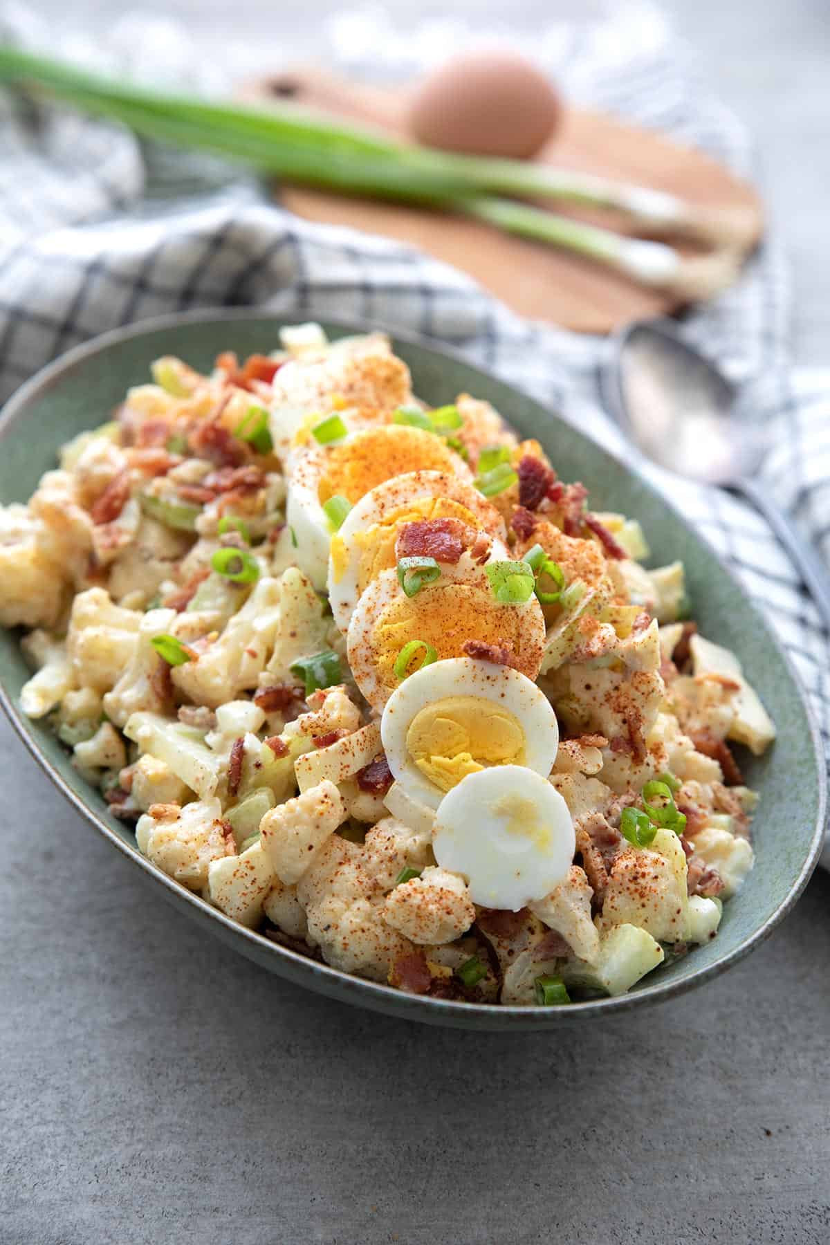 Cauliflower Potato Salad in a green oval serving dish with sliced hard boiled egg on top.