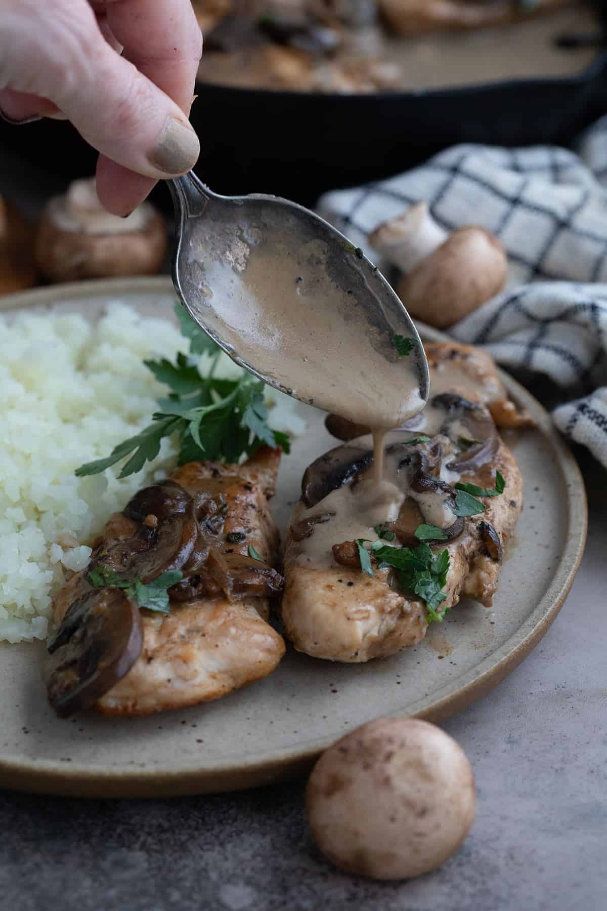 A spoon drizzling marsala sauce over chicken on a plate.