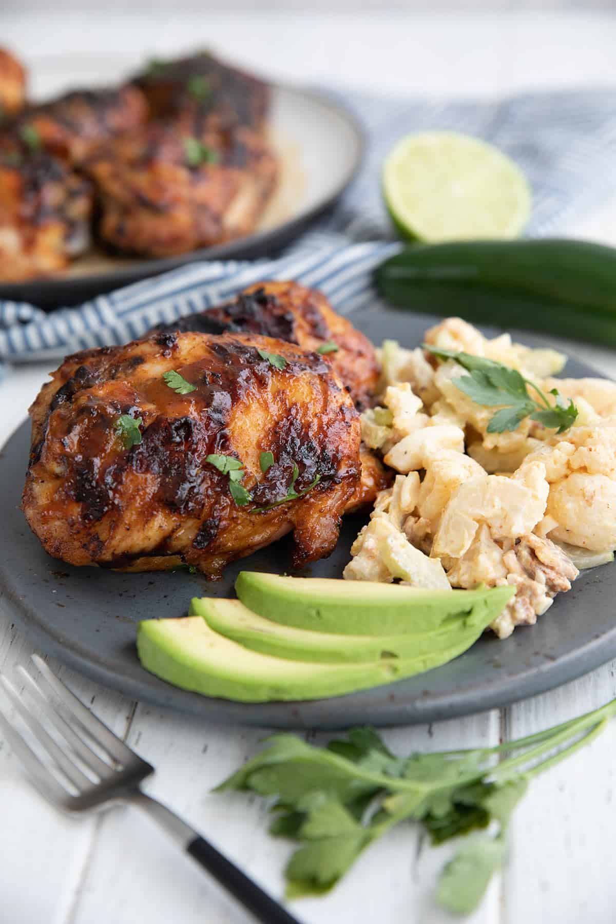Two chipotle lime chicken thighs on a gray plate with cauliflower potato salad and avocado.