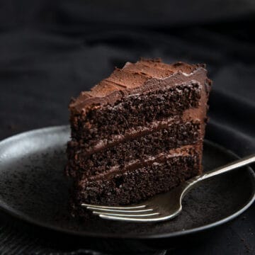 A slice of dark chocolate keto cake on a black plate on a black table.