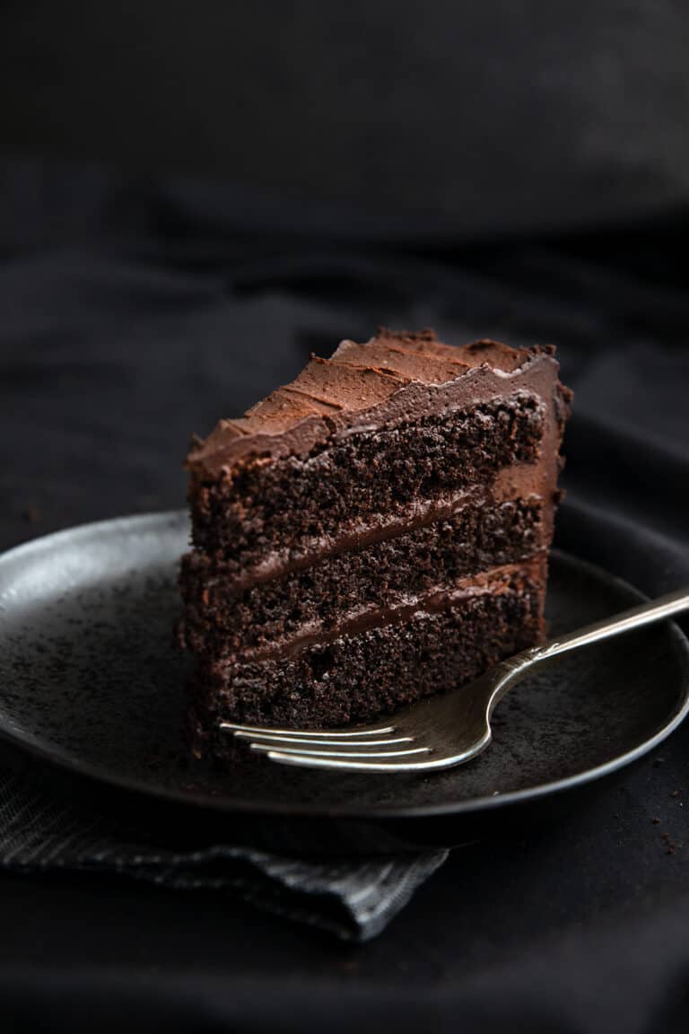 A slice of dark chocolate keto cake on a black plate on a black table.