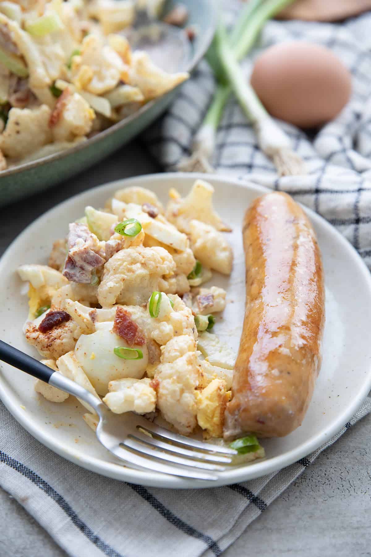 Cauliflower potato salad and a grilled sausage on a plate with a fork.