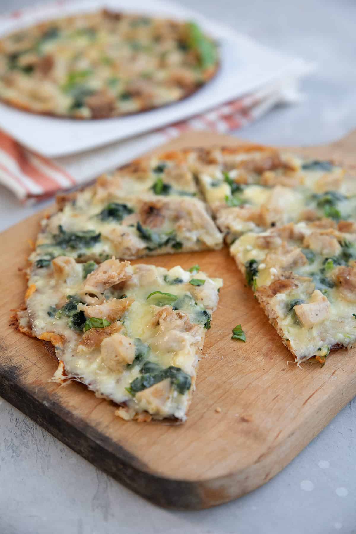 Keto Chicken Alfredo Pizza cut up on a wooden cutting board with another pizza in the background.