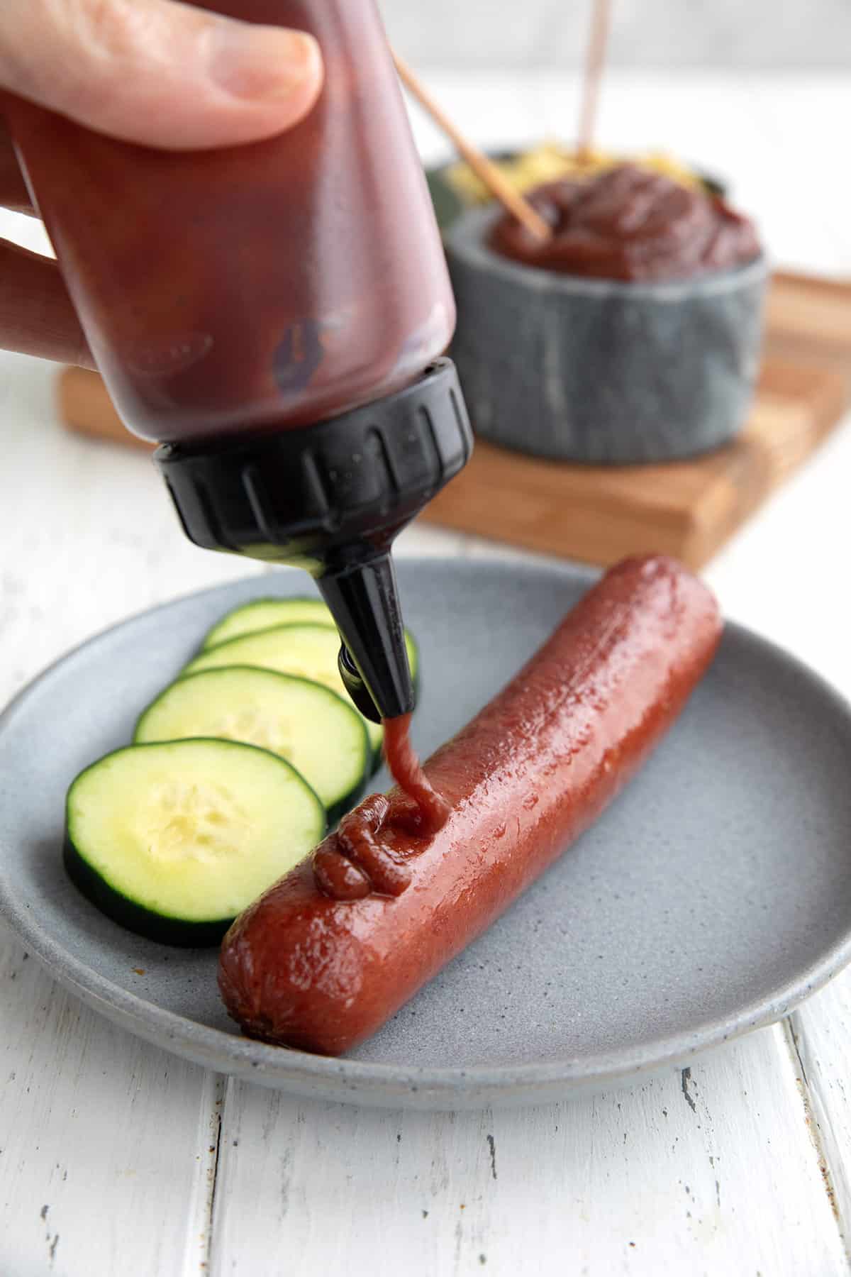 A squeeze bottle filled with sugar free ketchup being squeezed over a hot dog.