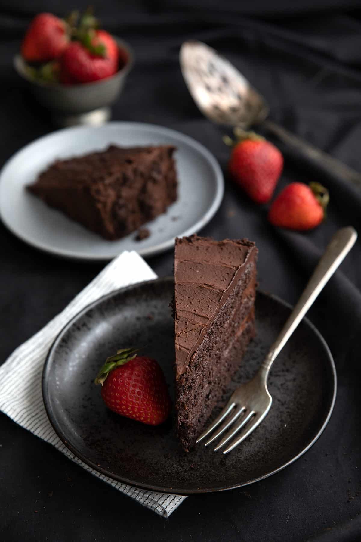 A slice of keto chocolate cake on a black plate with a strawberry and a fork.