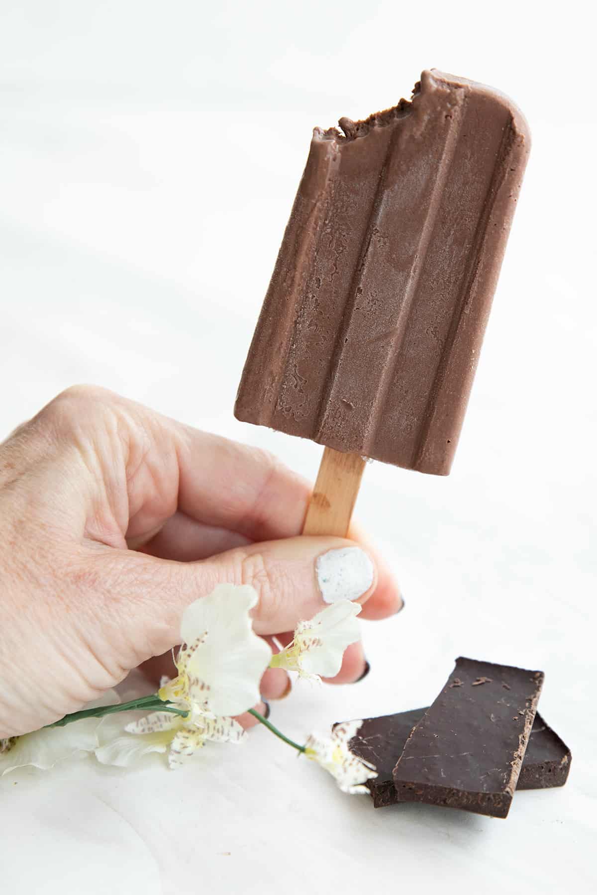 A hand holding up a sugar free fudgesicle with a bite taken out of the corner.