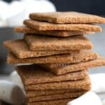 Titled image of a stack of keto graham crackers surrounded by keto marshmallows and pieces of chocolate.