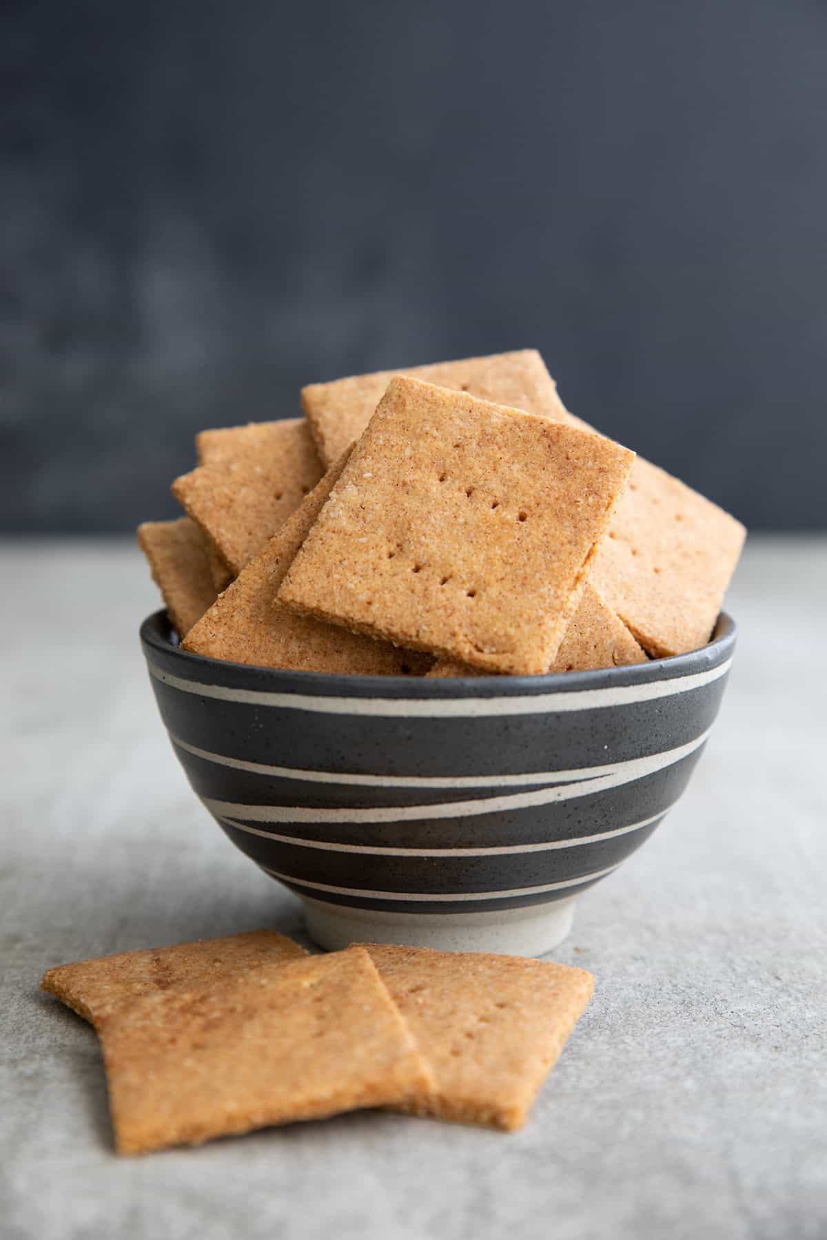 Sugar free keto graham crackers in a black patterned bowl on a gray table.