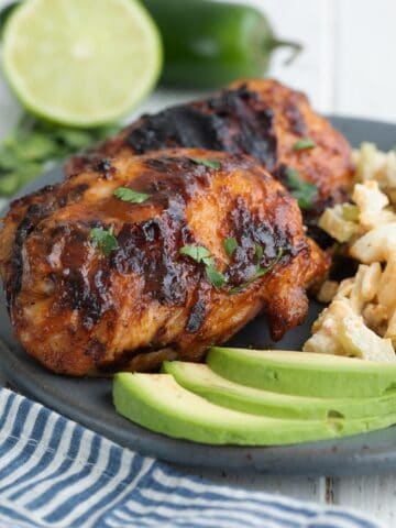 Close up shot of chipotle lime chicken on a gray plate with lime and jalapeño in the background.