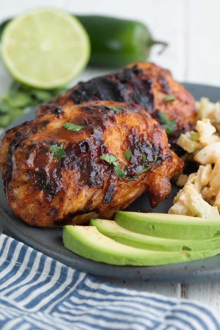 Close up shot of chipotle lime chicken on a gray plate with lime and jalapeño in the background.