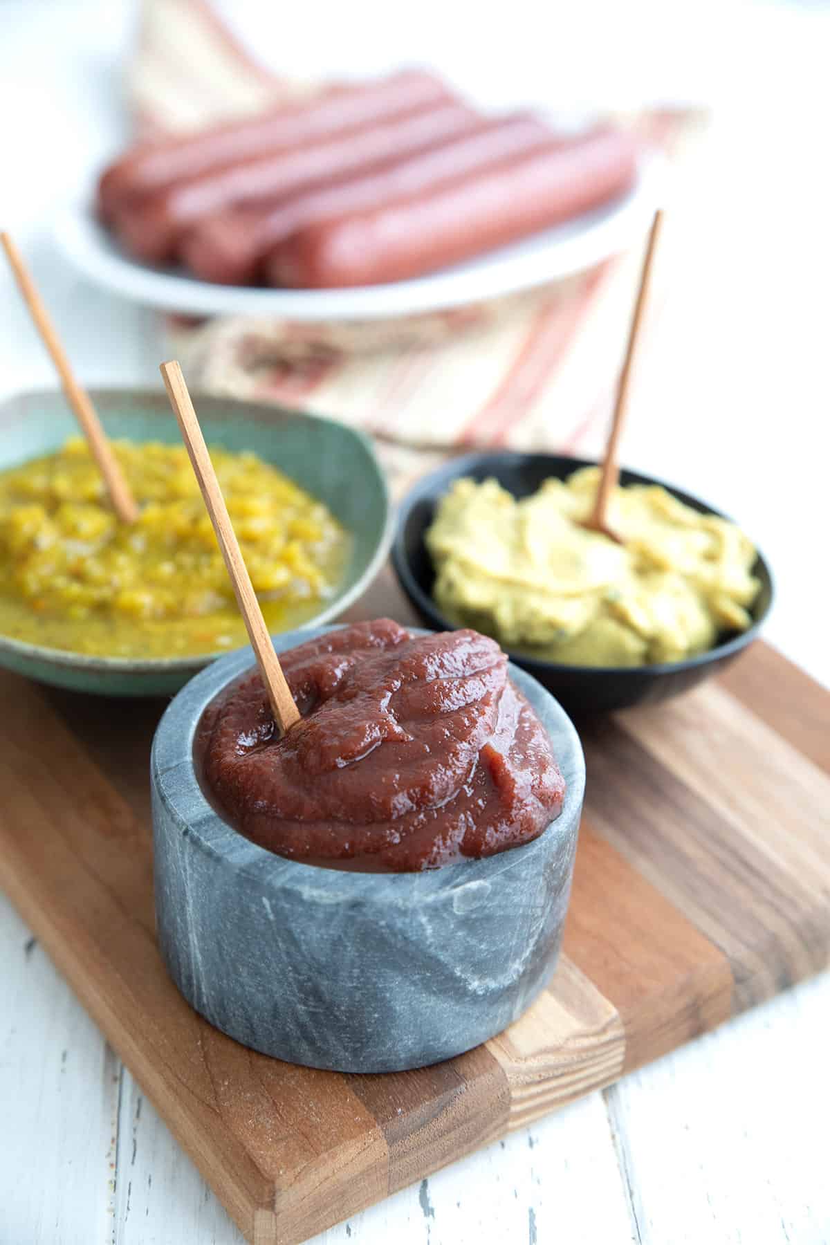 Sugar free ketchup and other condiments in bowls on a wooden cutting board.