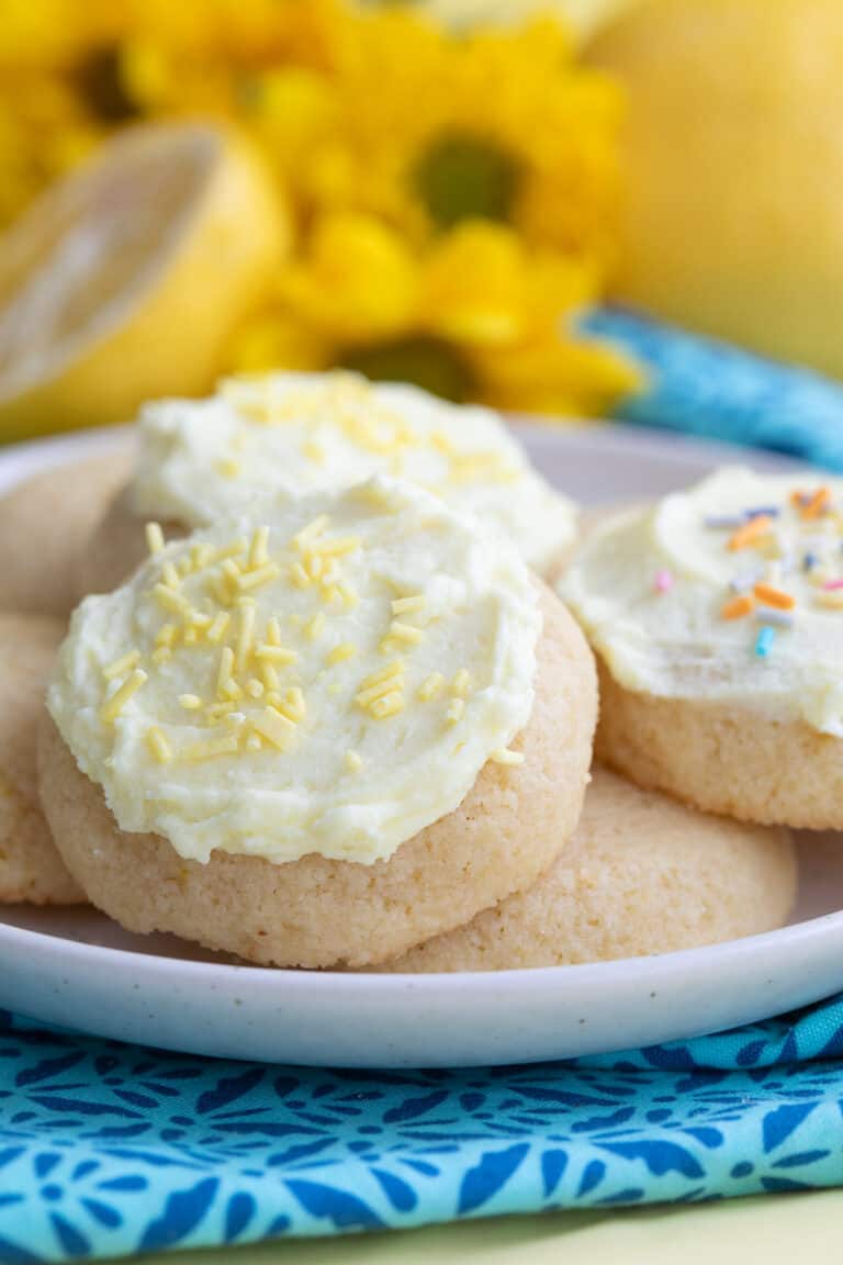 Close up shot of keto lemon cookies piled up on a plate over a teal and blue napkin.