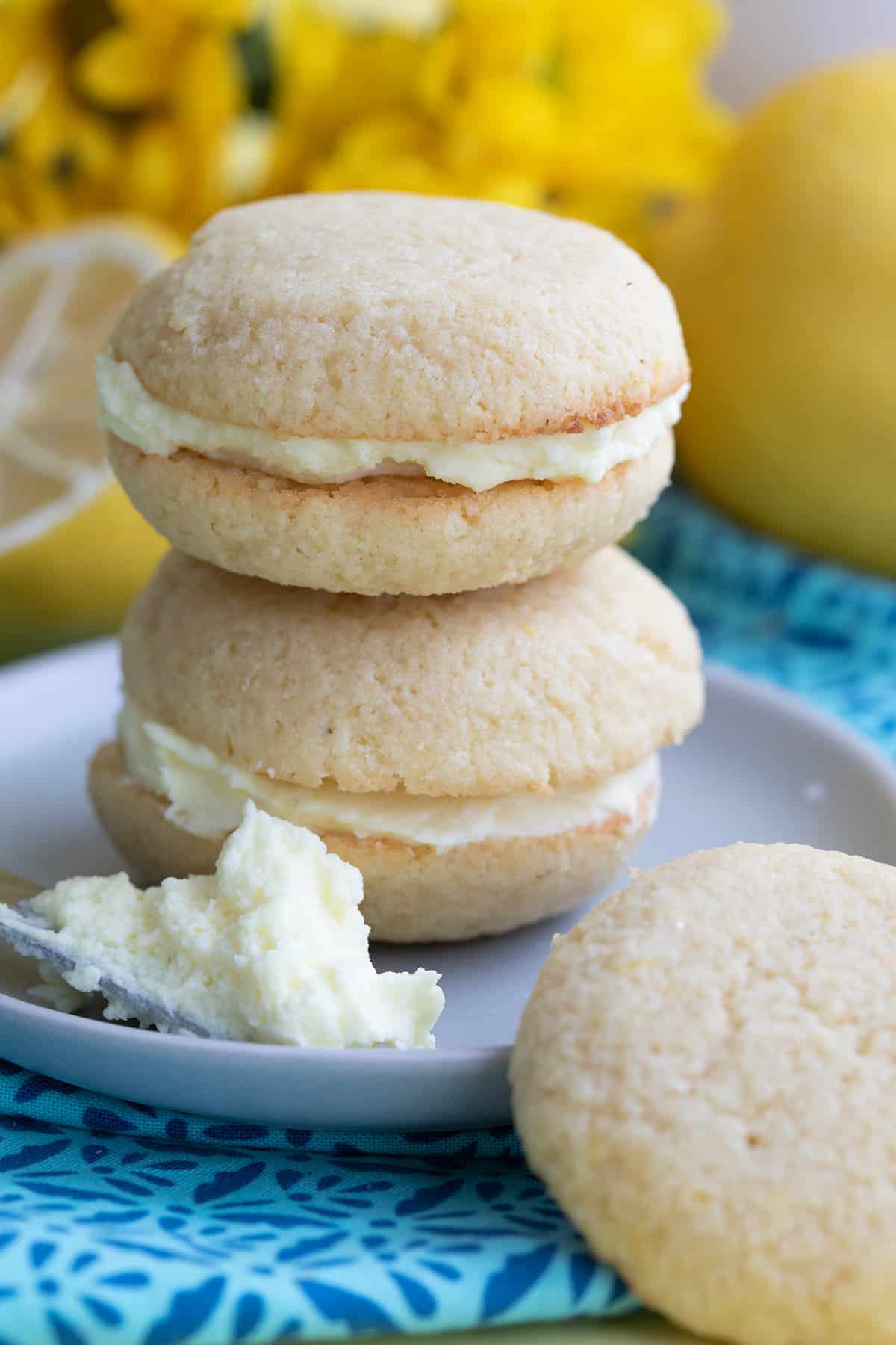 Two keto lemon cream sandwich cookies in a stack on a plate, with a knife with frosting on it.